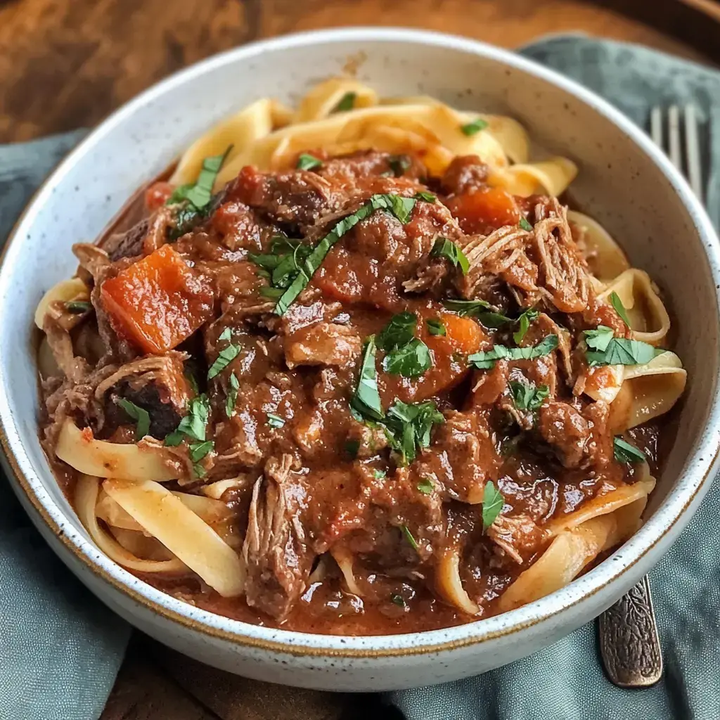 Assiette de fettuccine nappées d’une sauce à la viande fondante avec carottes et herbes fraîches.