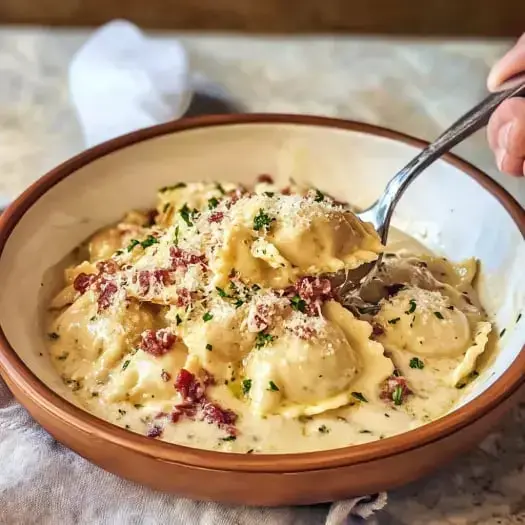 Un bol de raviolis crémeux garni de morceaux de bacon et de persil, avec une fourchette qui en prélève quelques-uns.