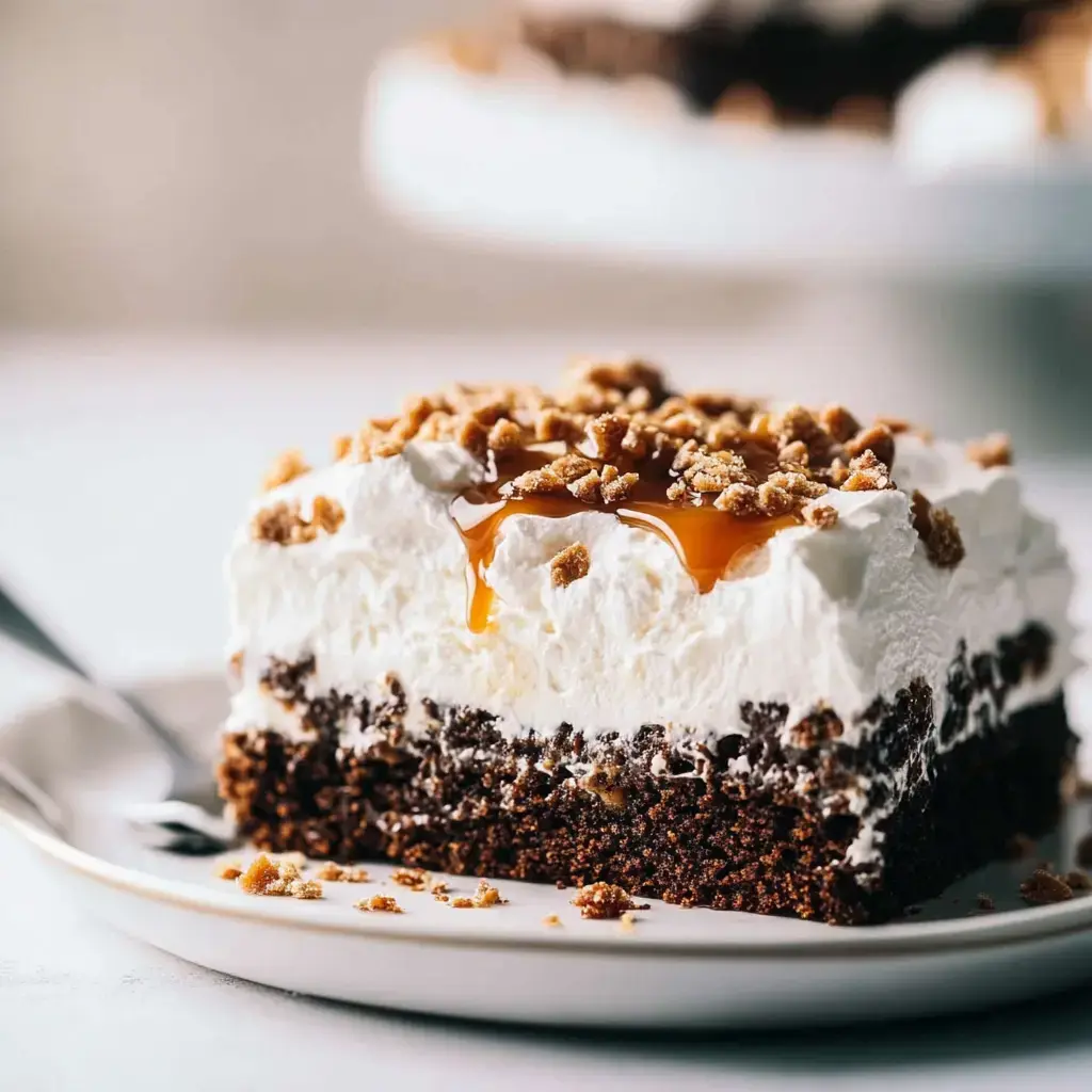 Une part de gâteau chocolat garnie de crème fouettée et nappée de caramel, surmontée de biscuits émiettés, sur une assiette blanche.