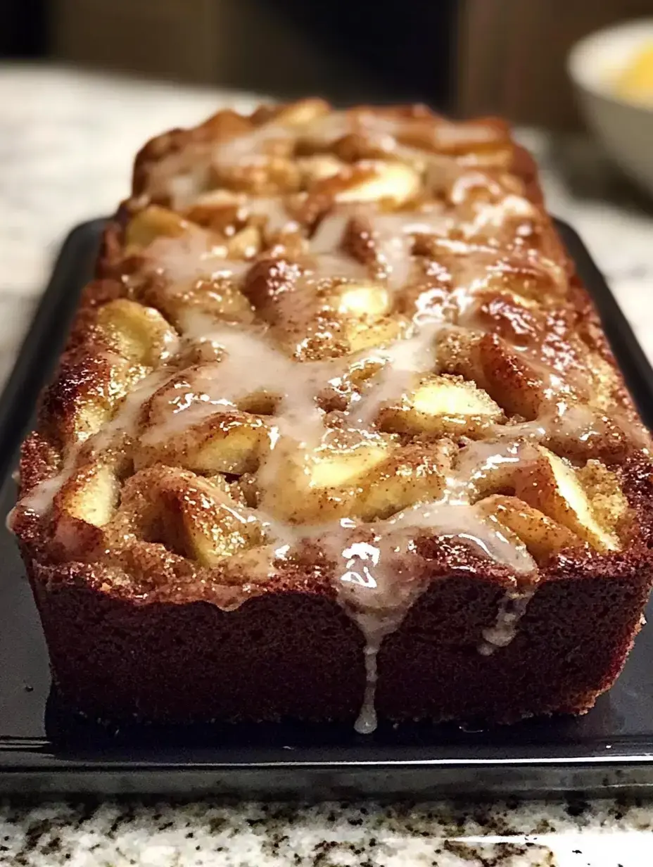 Un gâteau fraîchement cuit recouvert d'un glaçage et de morceaux de pomme, présenté sur un plateau de service foncé.