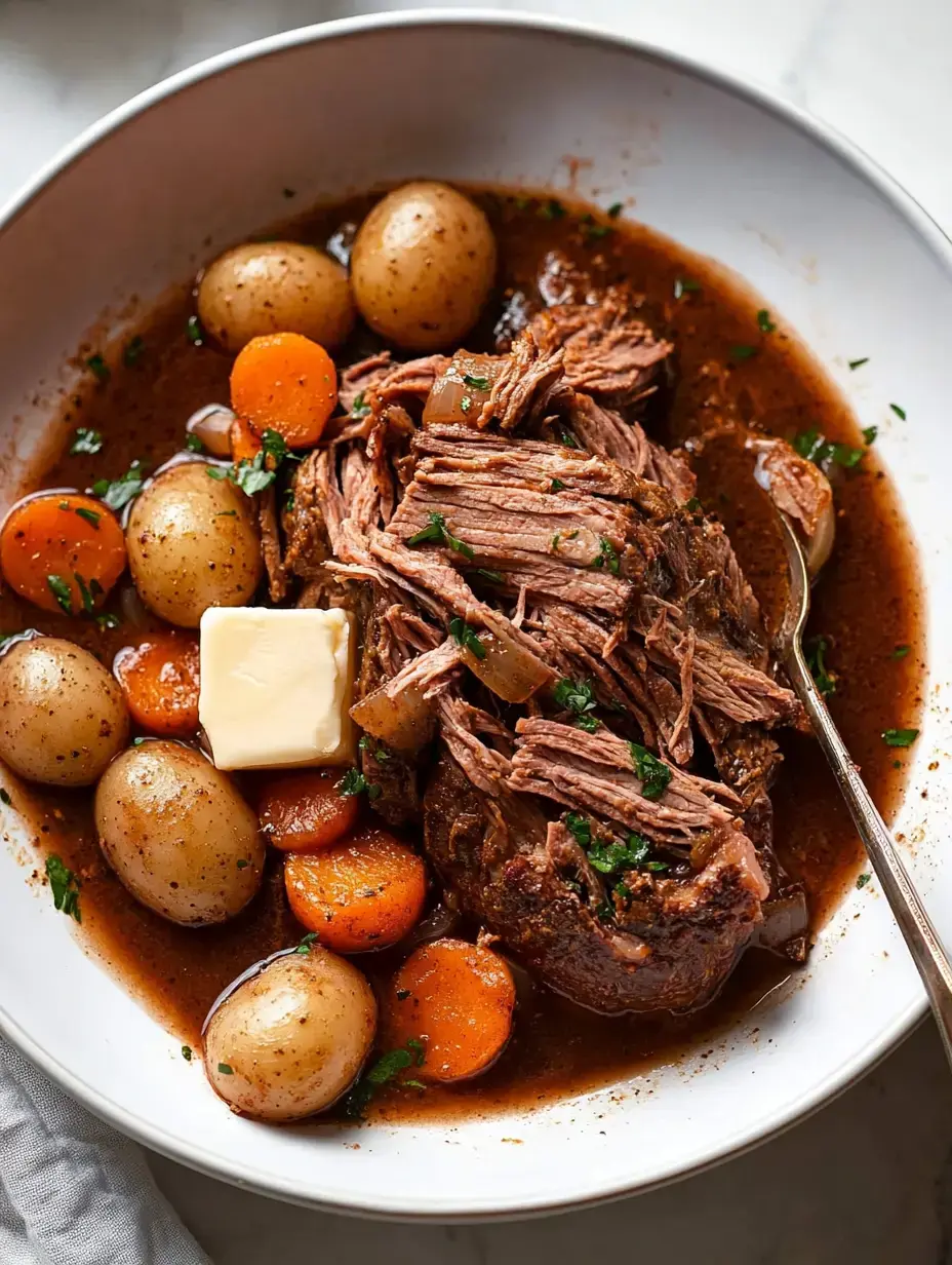 Une portion de bœuf tendre effiloché avec des pommes de terre nouvelles et des carottes, surmontée d'une noisette de beurre et garnie de persil dans un bol blanc.