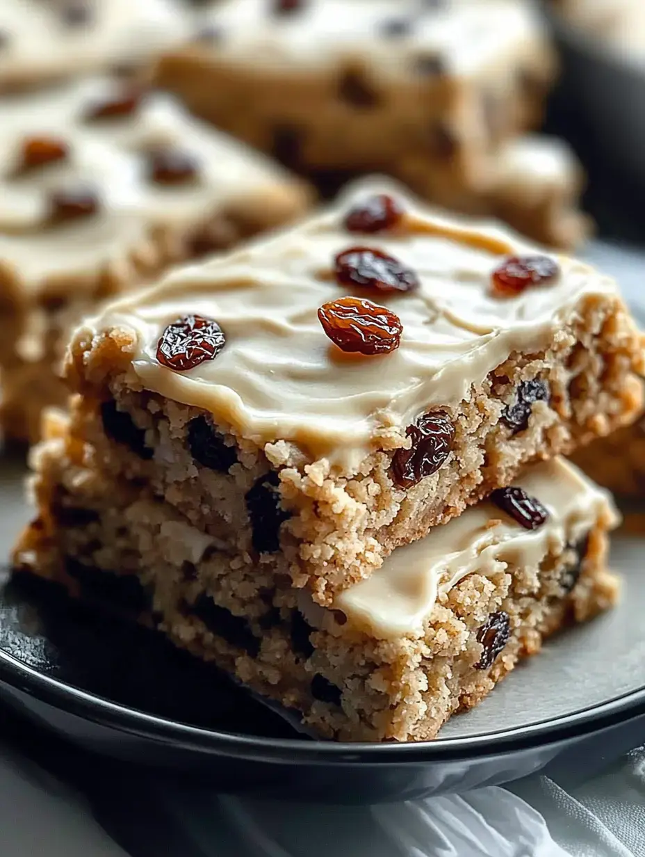 Un gros plan de deux morceaux empilés de gâteau glacé avec des raisins secs sur le dessus, présentés sur une assiette noire.