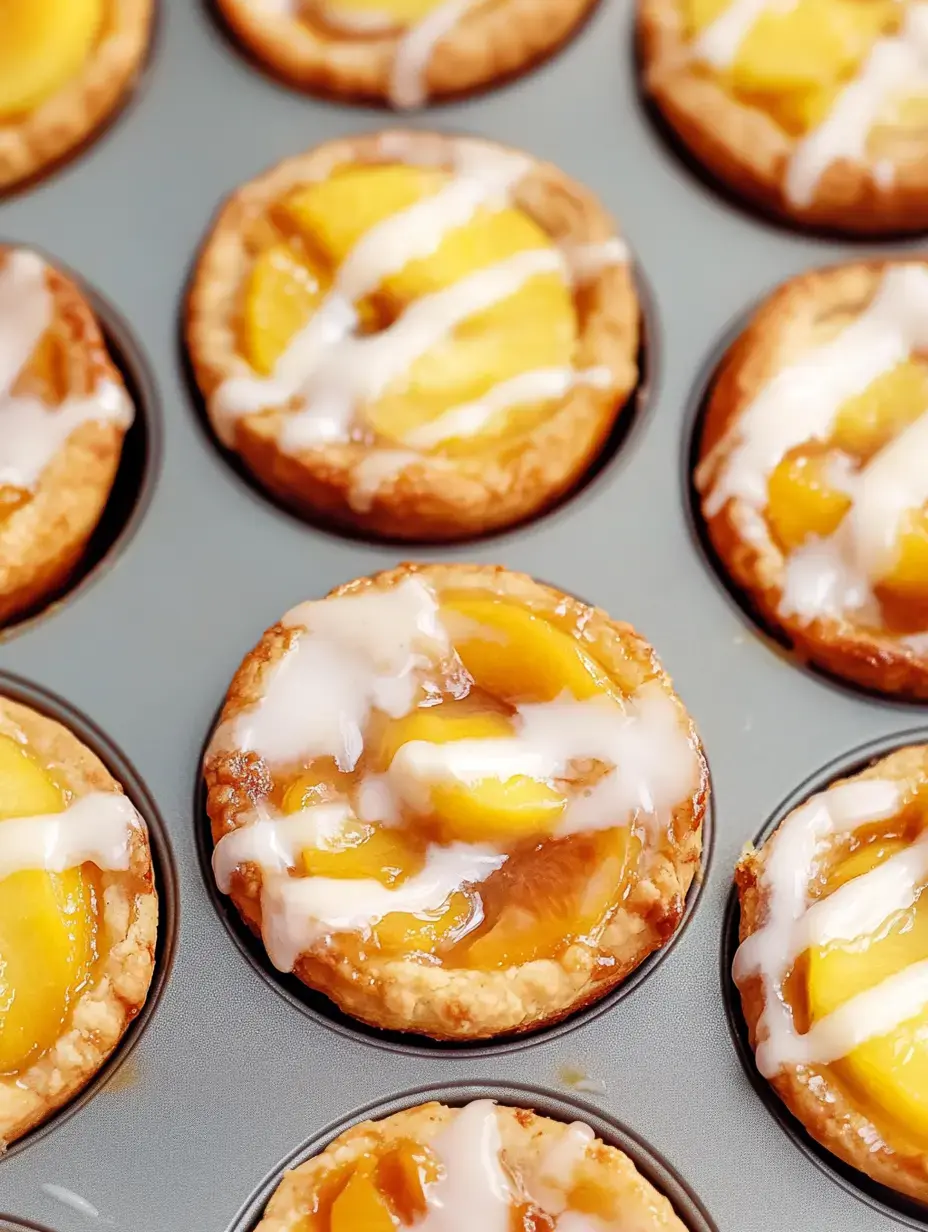 Un gros plan de mini tartelettes aux fruits avec des tranches de pêche et un filet de glaçage, disposées dans un moule à muffins.