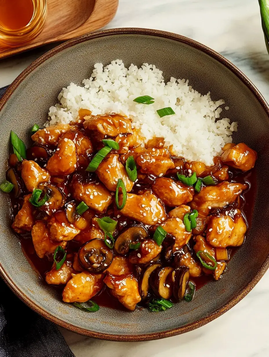 Un bol de poulet croustillant enrobé d'une sauce savoureuse, servi avec du riz blanc et garni d'oignons verts hachés et de champignons.