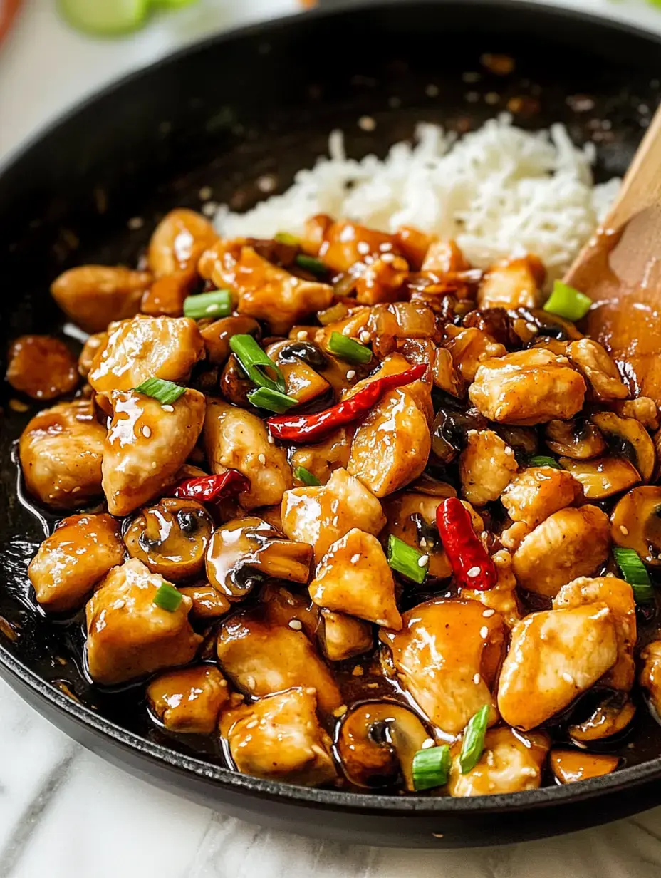 Un gros plan d'une poêle remplie de morceaux de poulet sautés, de champignons et d'oignons verts dans une sauce foncée, servis avec du riz blanc.