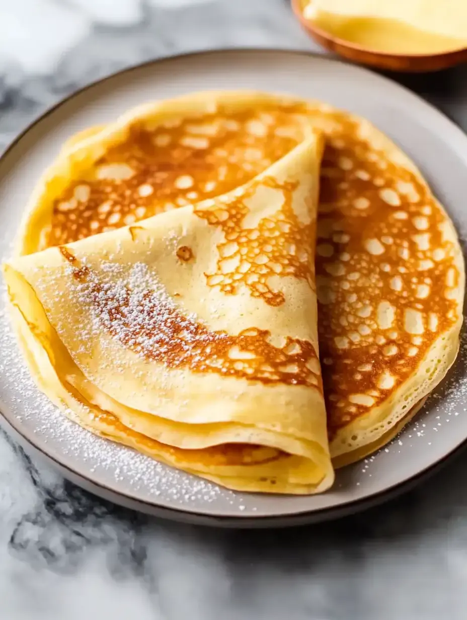 Une assiette de crêpes dorées fraîchement préparées saupoudrées de sucre glace.